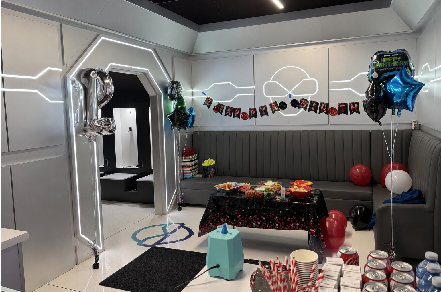 NextGen VR party lounge decorated for a birthday — sci-fi LED walls, lounge seating, balloons and snack table